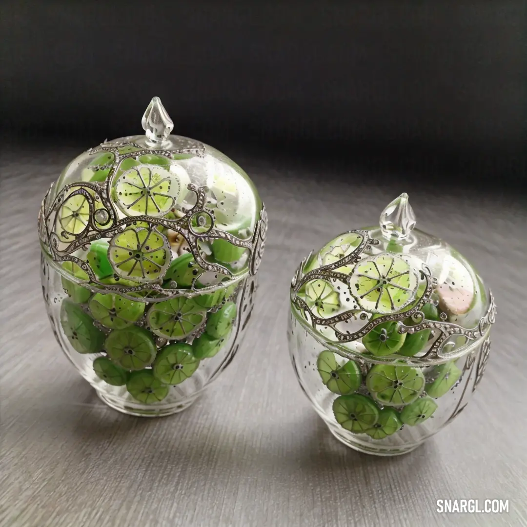 Couple of glass vases filled with green fruit and vegetables on a table top with a black background. Example of CMYK 25,0,42,23 color.