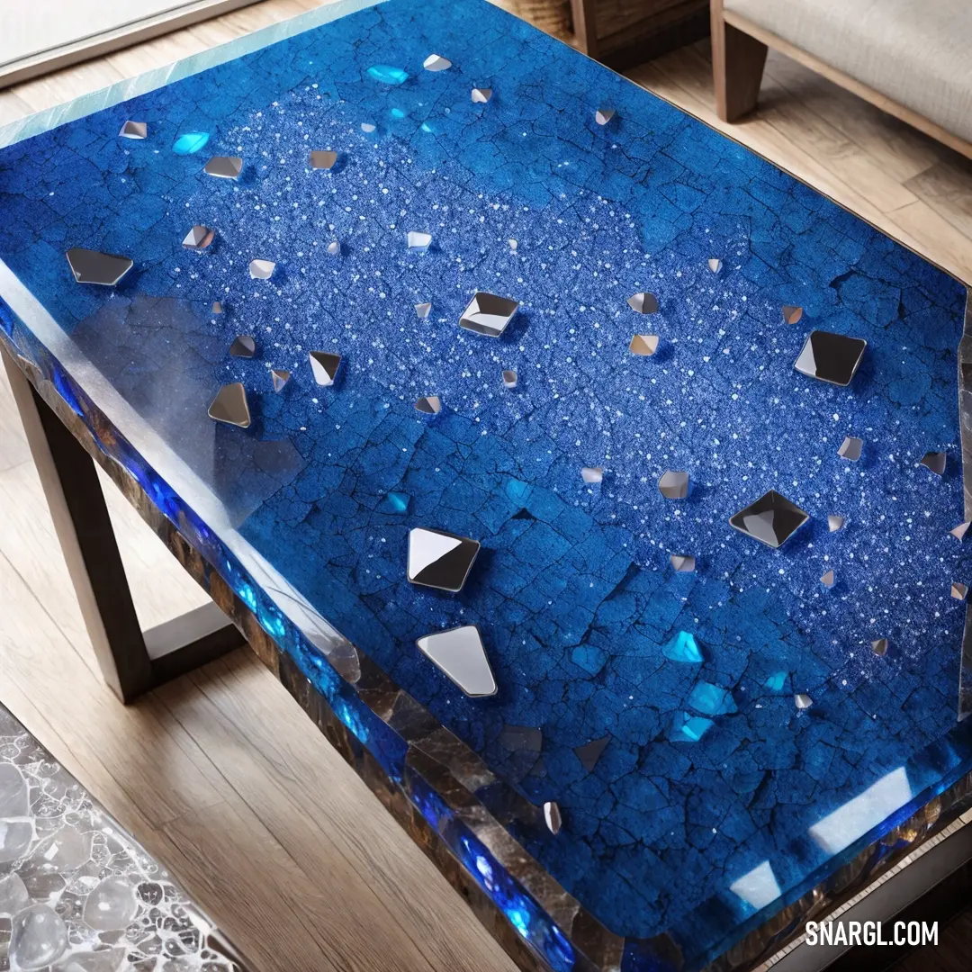 Blue table with a glass top and silver accents on it, with a couch in the background. Example of RGB 0,49,83 color.