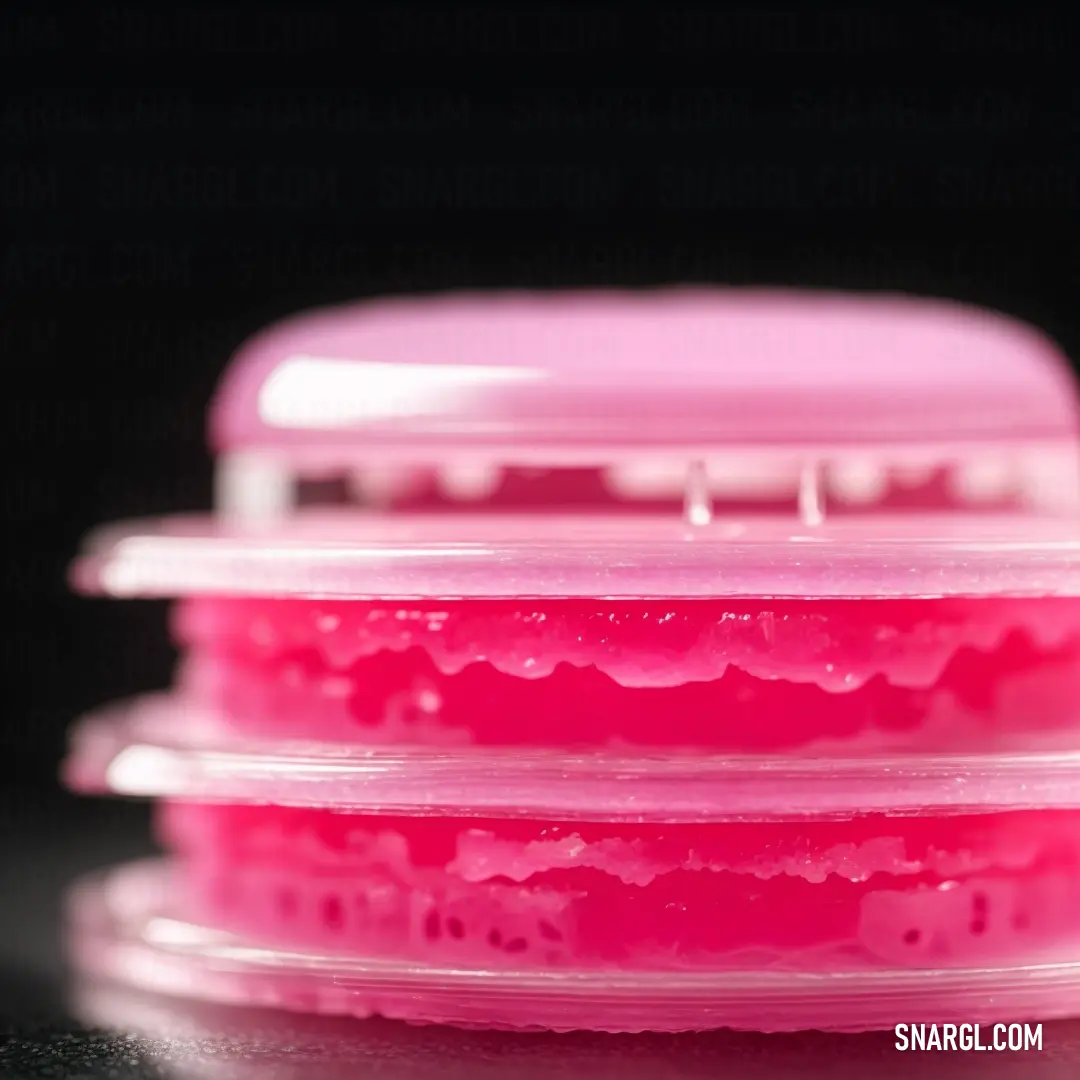Three plastic containers with pink lids on a table top with a black background