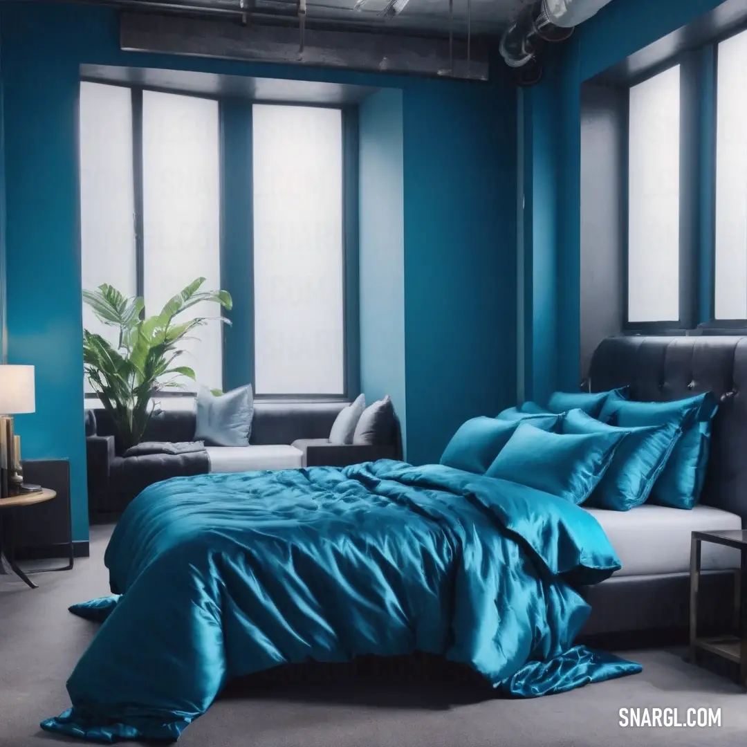 Bed with a blue comforter and pillows in a room with a couch and a window with a plant. Example of #0072A3 color.