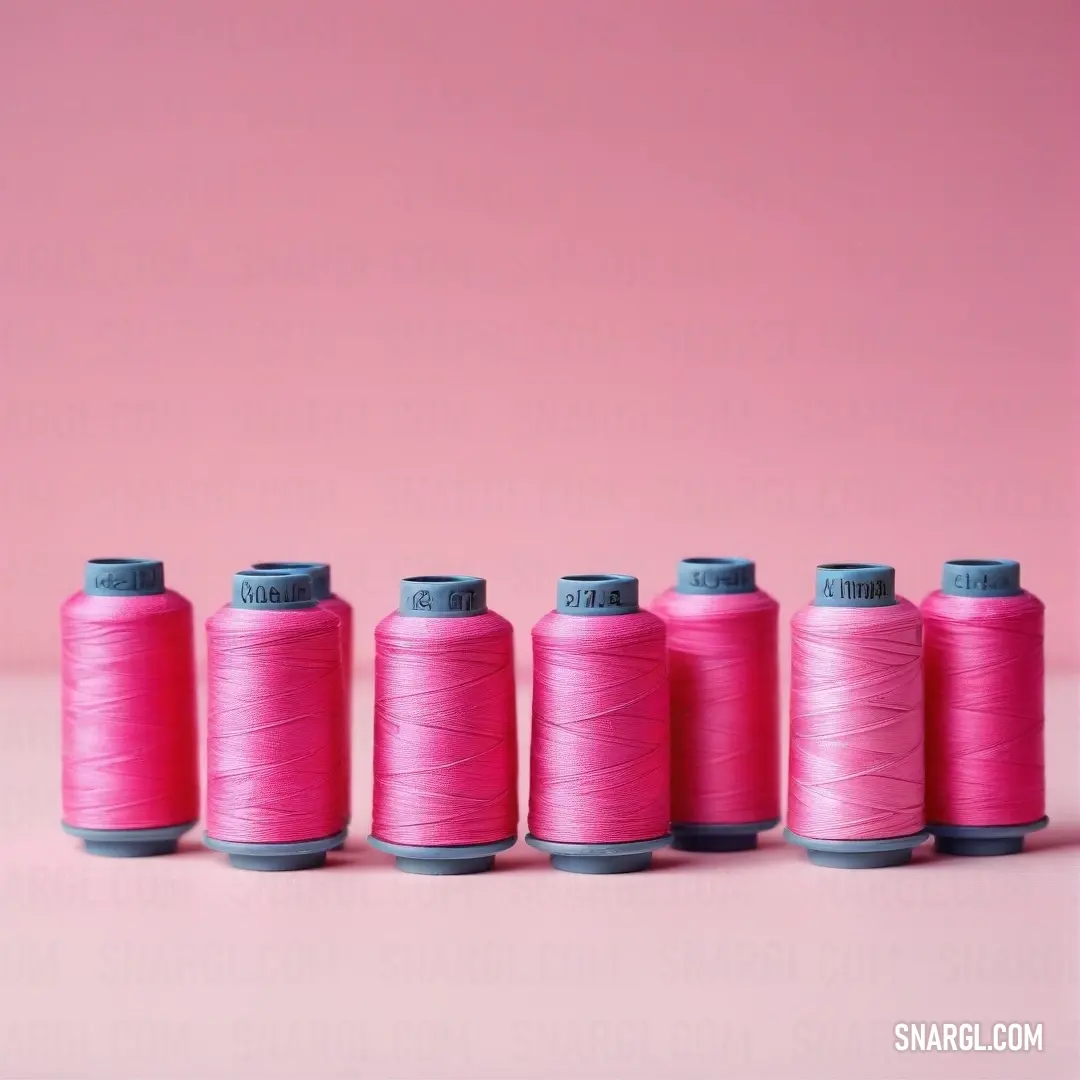 A vibrant row of pink spools of thread stands out against a soft pink background, creating a harmonious blend of textures and colors that beckons to crafters and sewing enthusiasts alike.