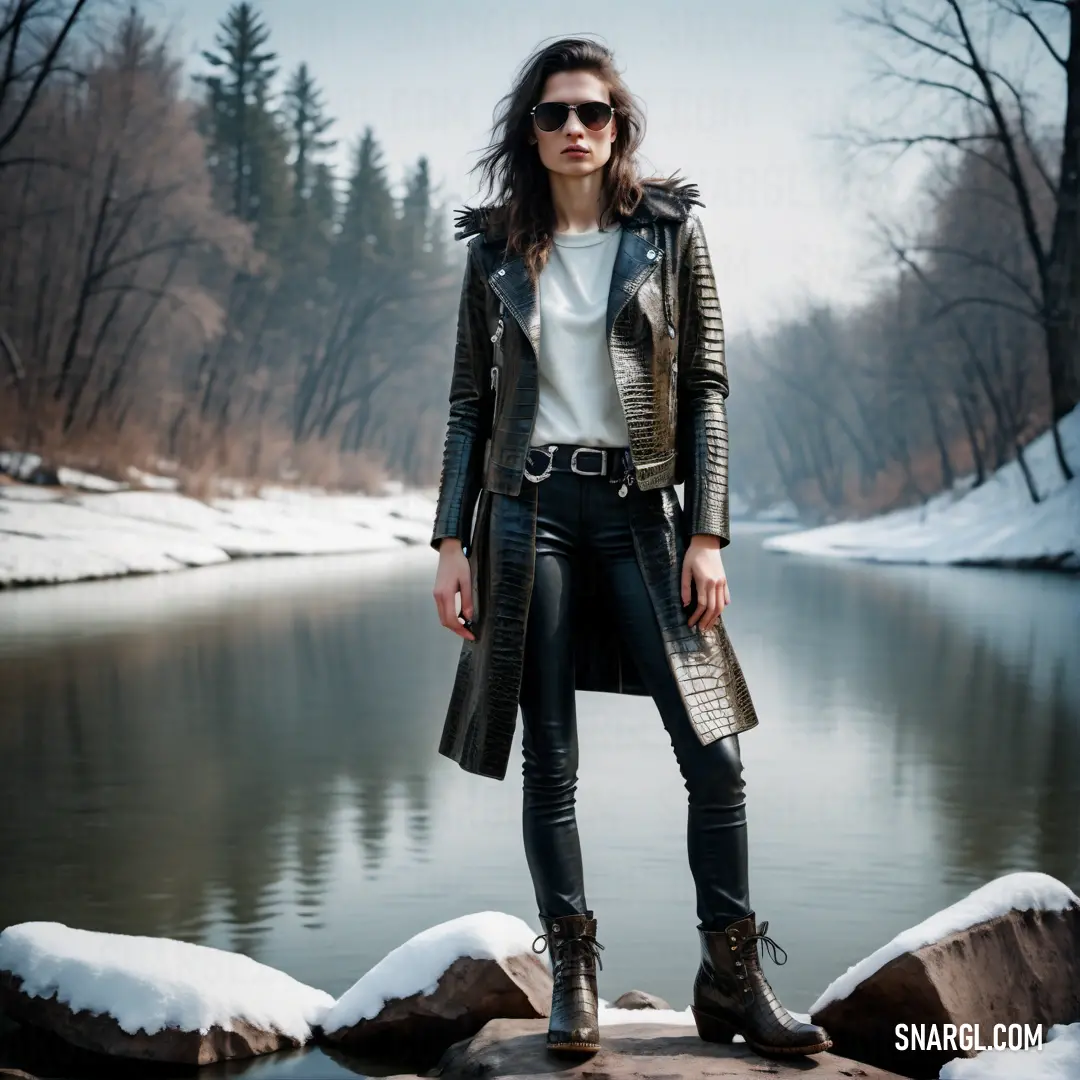 Woman standing on a rock near a river wearing a leather jacket and boots with a white shirt and black pants