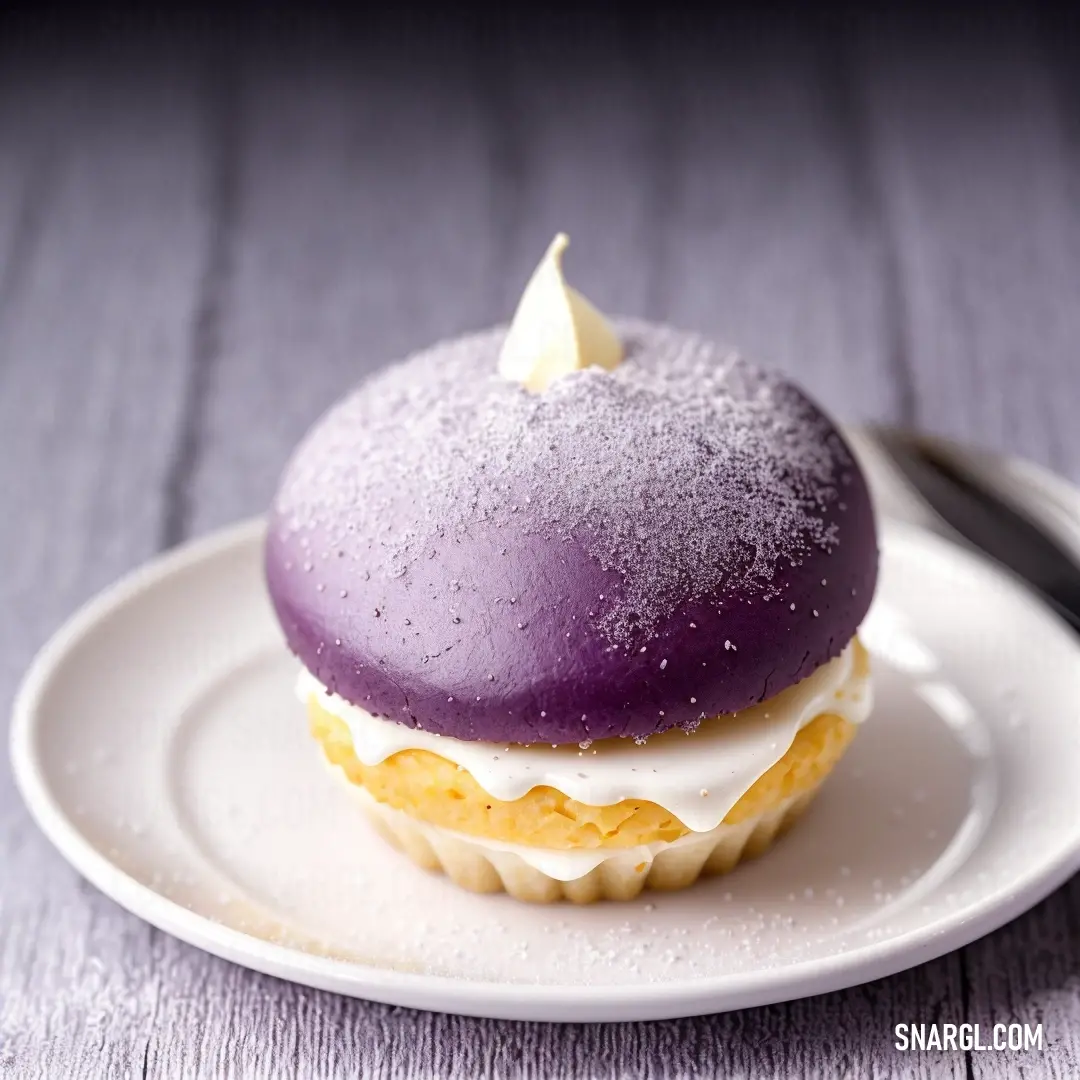 Purple frosted cupcake on a white plate with a fork and knife on the side of the plate