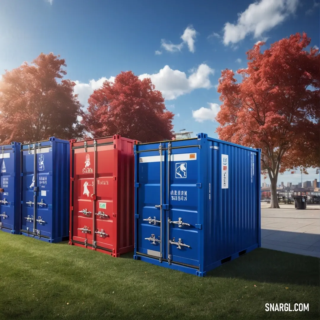 Royal azure color. Row of blue and red shipping containers on top of a lush green field next to a tree