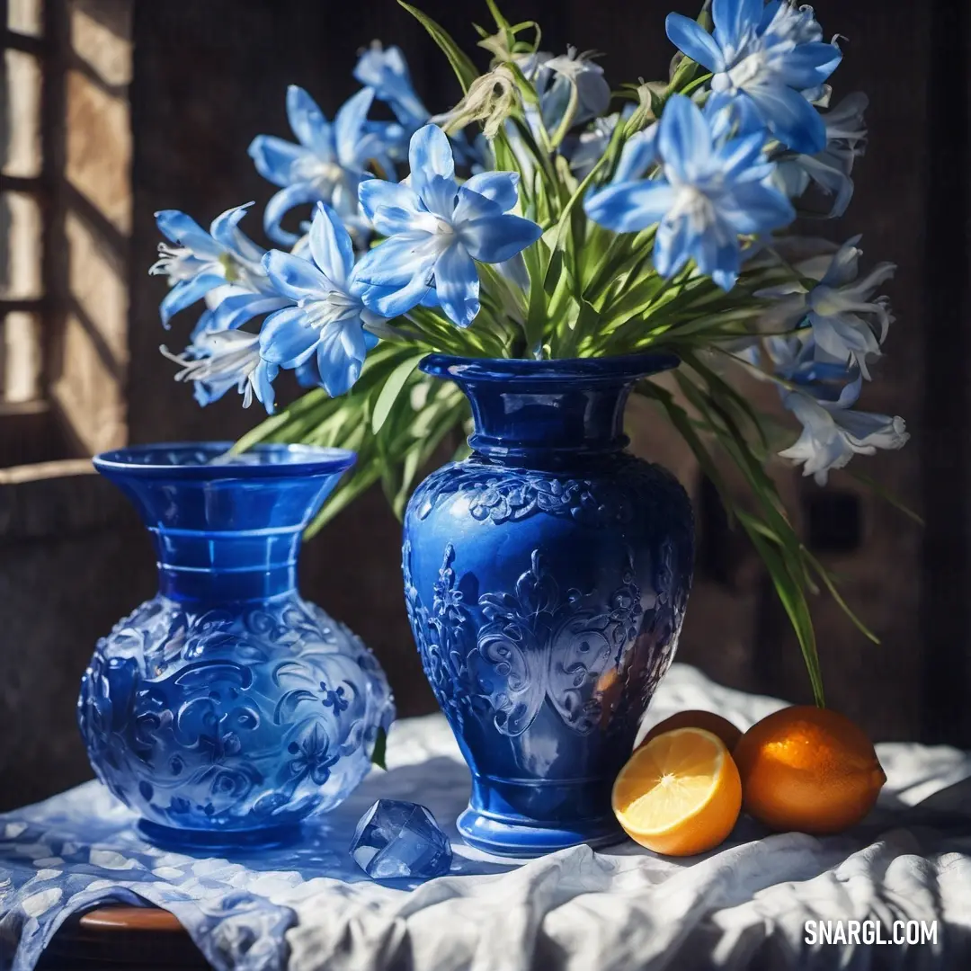 Blue vase with flowers and oranges on a table cloth next to a window with a curtain. Example of Royal azure color.