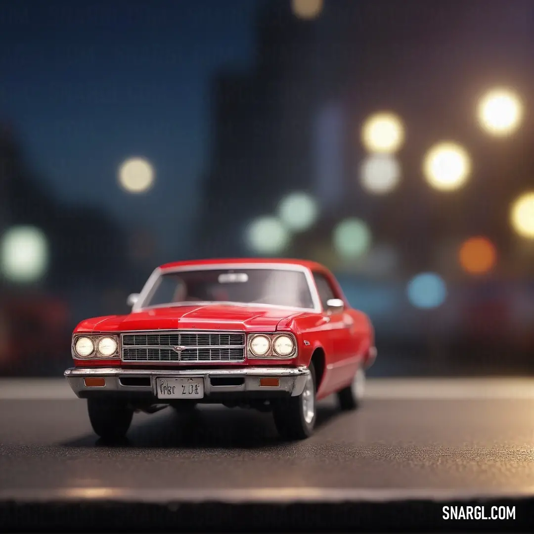 Red toy car is on a street at night time with lights in the background. Example of RGB 255,0,40 color.
