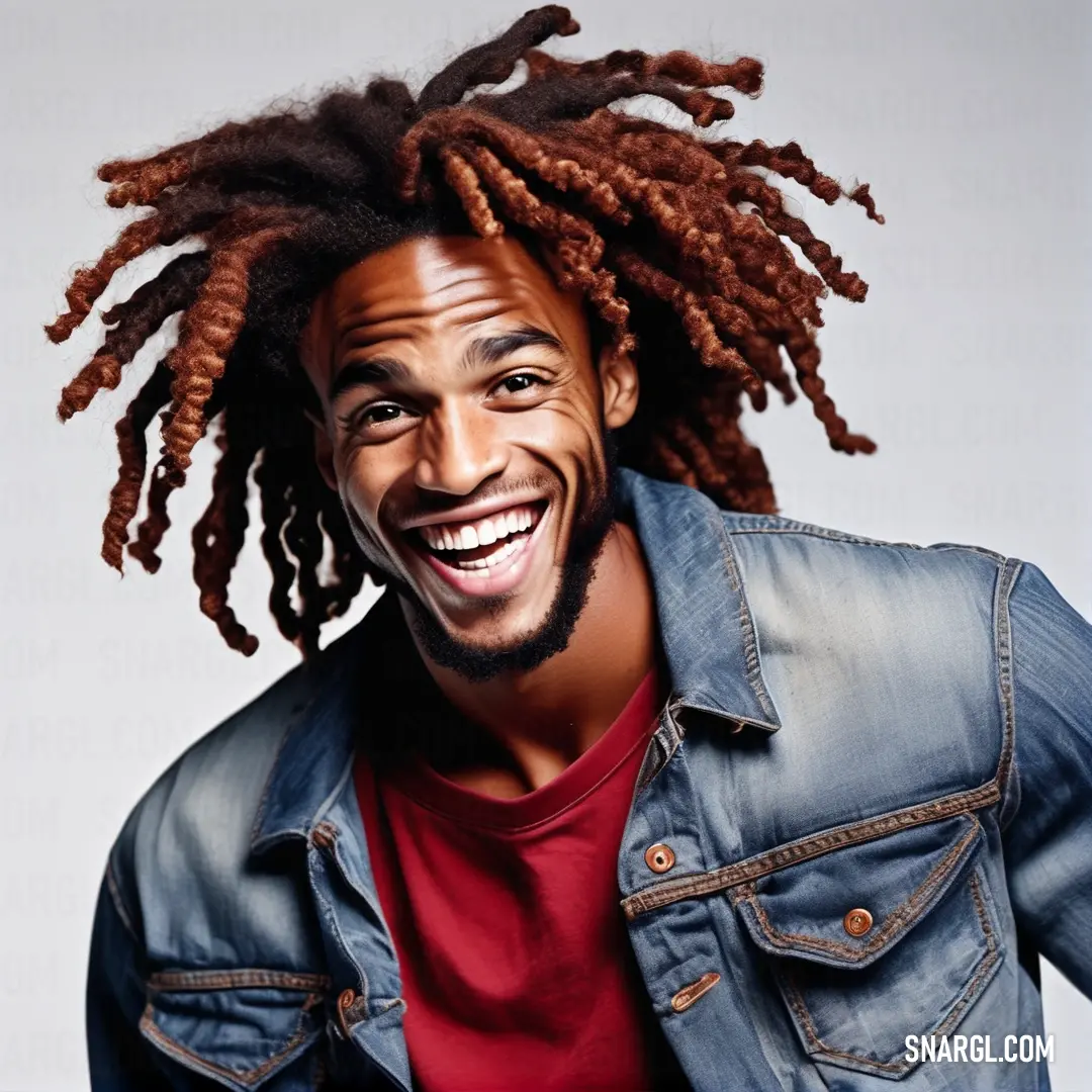 Man with dreadlocks smiling and wearing a denim jacket and red shirt. Color Rufous.
