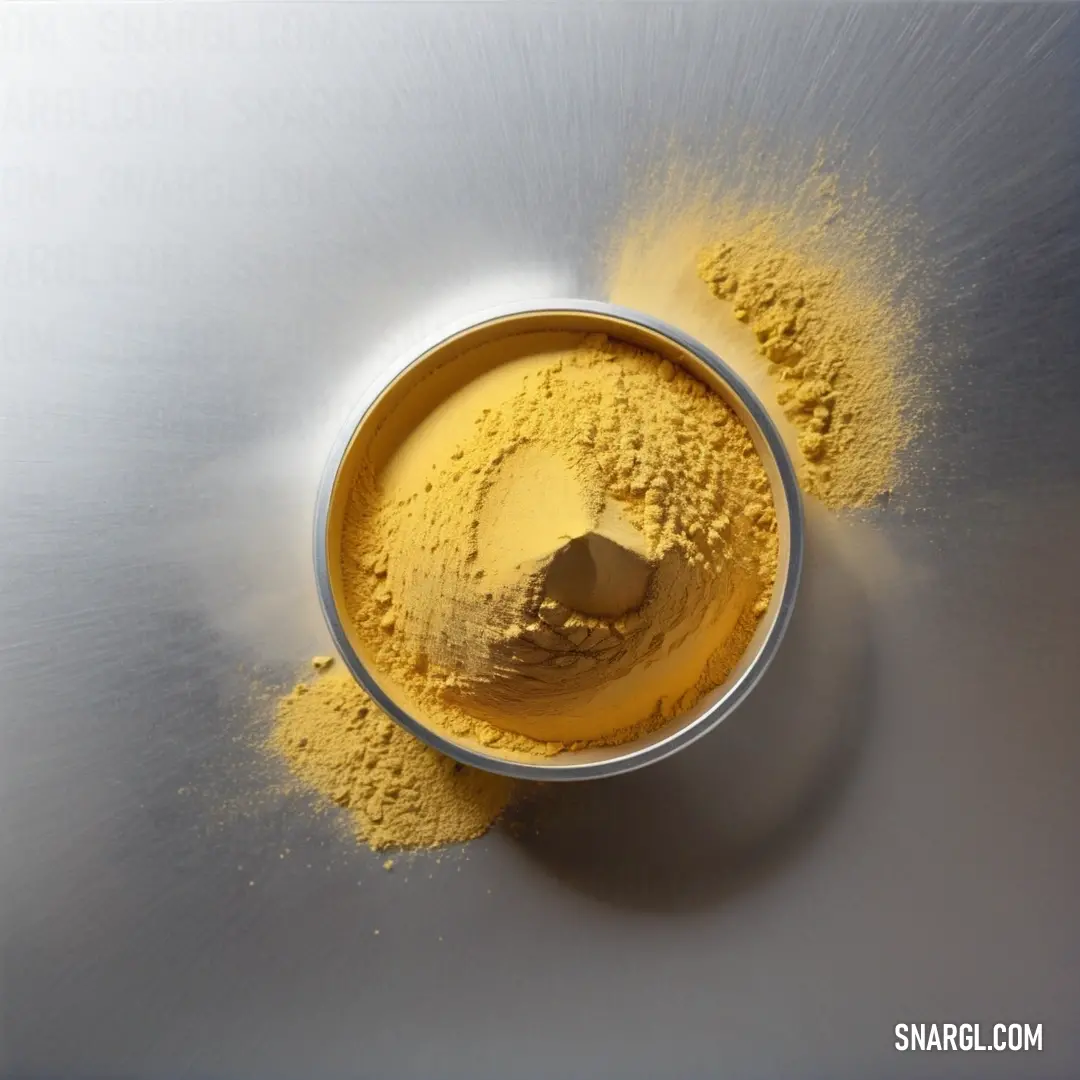 Metal bowl filled with yellow powder on top of a table top next to a spoon. Color CMYK 0,21,74,20.