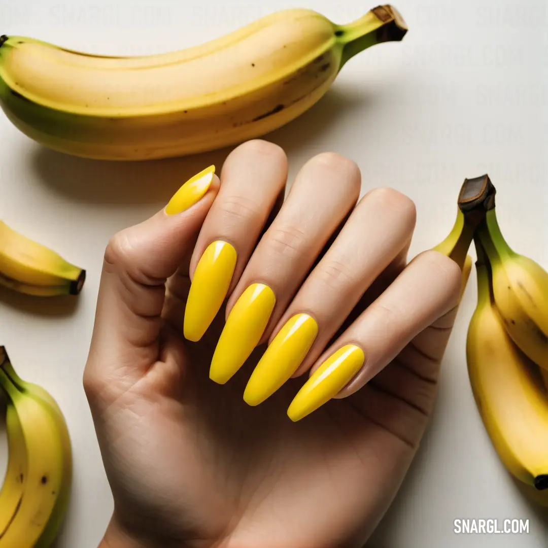 Woman's hand with yellow nails and yellow nail polish next to bananas on a white surface