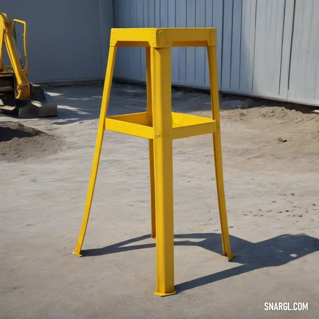 Yellow chair in the middle of a cement area next to a building and a bulldozer. Color School bus yellow.