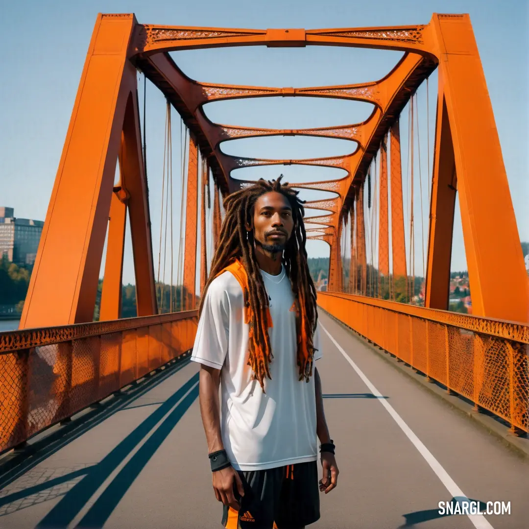 Man with dreadlocks standing on a bridge over water with a city in the background