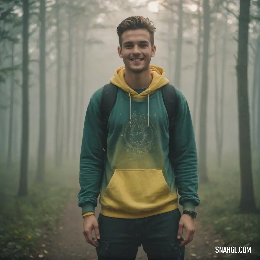 Man standing in the woods wearing a yellow and green hoodie and smiling at the camera with a foggy background