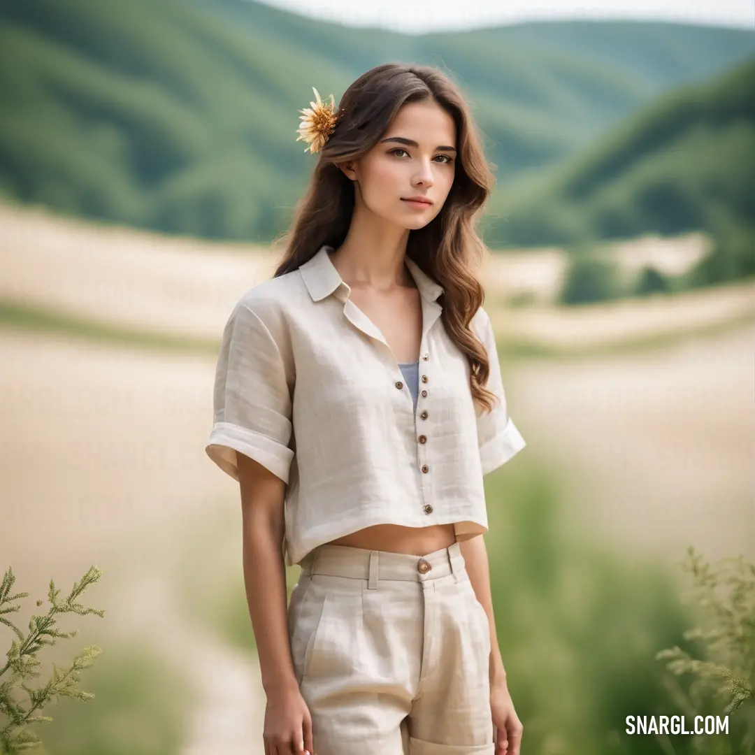 Woman standing in a field with a flower in her hair and a white shirt on her shoulders and a mountain in the background