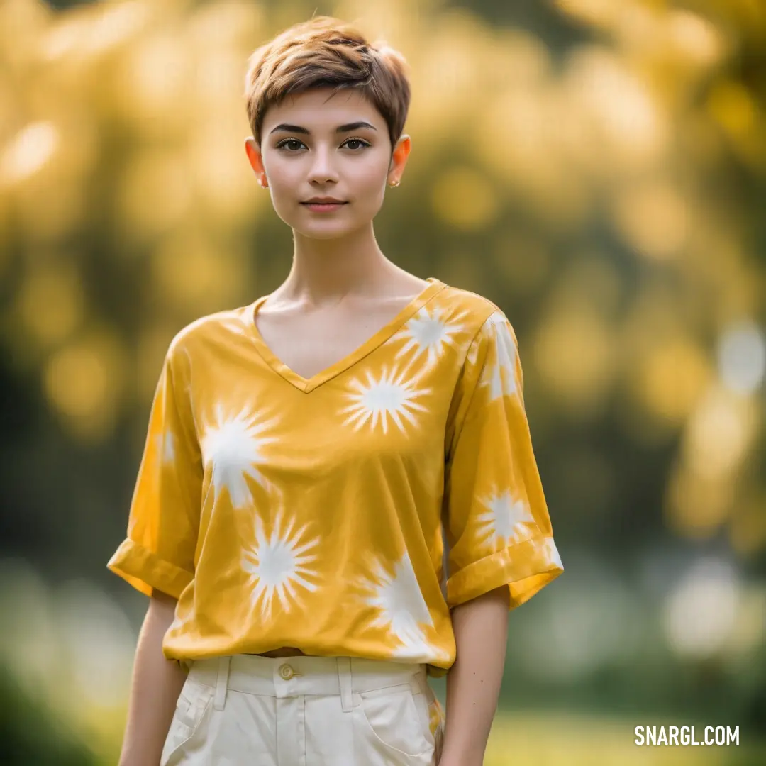 Woman with short hair wearing a yellow shirt and white shorts standing in a park with trees in the background