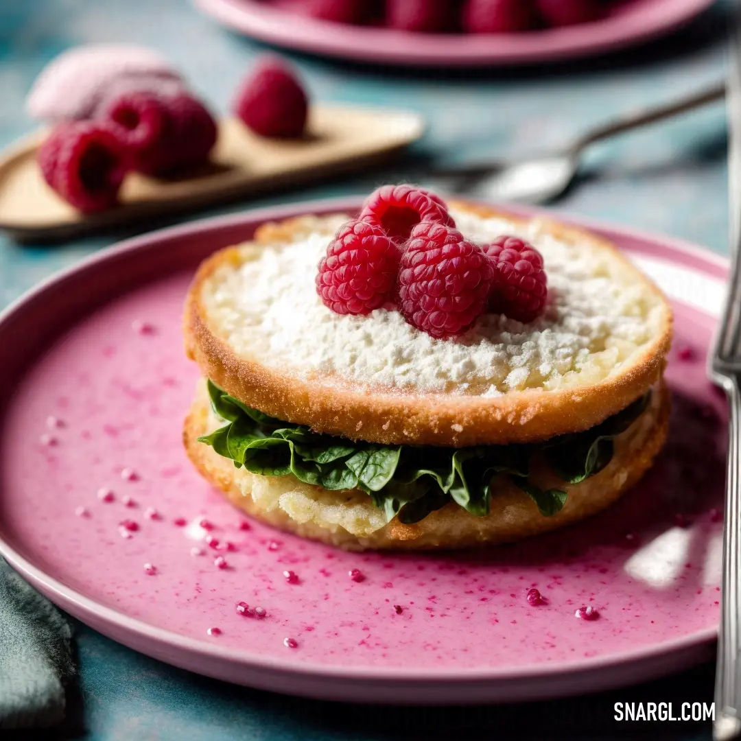 Sandwich with raspberries on top of it on a pink plate with a fork and spoon on the side
