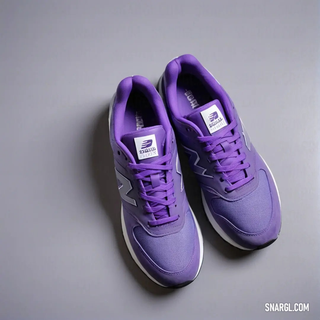 Pair of purple shoes on a gray surface with a white sole and a white top. Example of CMYK 40,44,0,25 color.