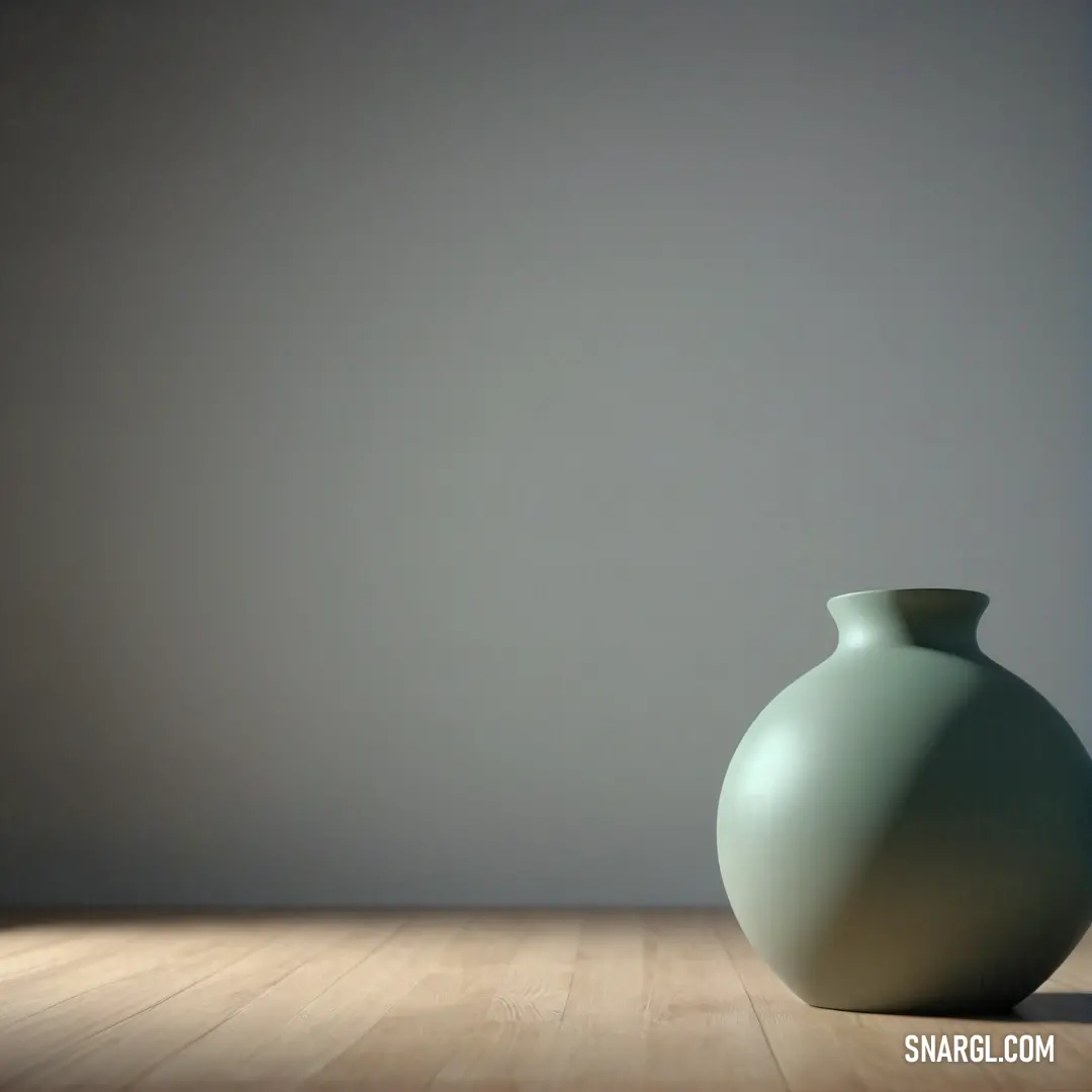 Green vase on a wooden table in a room with a white wall behind it and a window. Color CMYK 0,0,0,50.