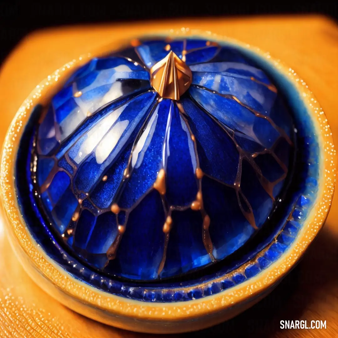 Ultramarine blue color. Blue bowl with a gold decoration on it on a table top with a wooden table top in the background