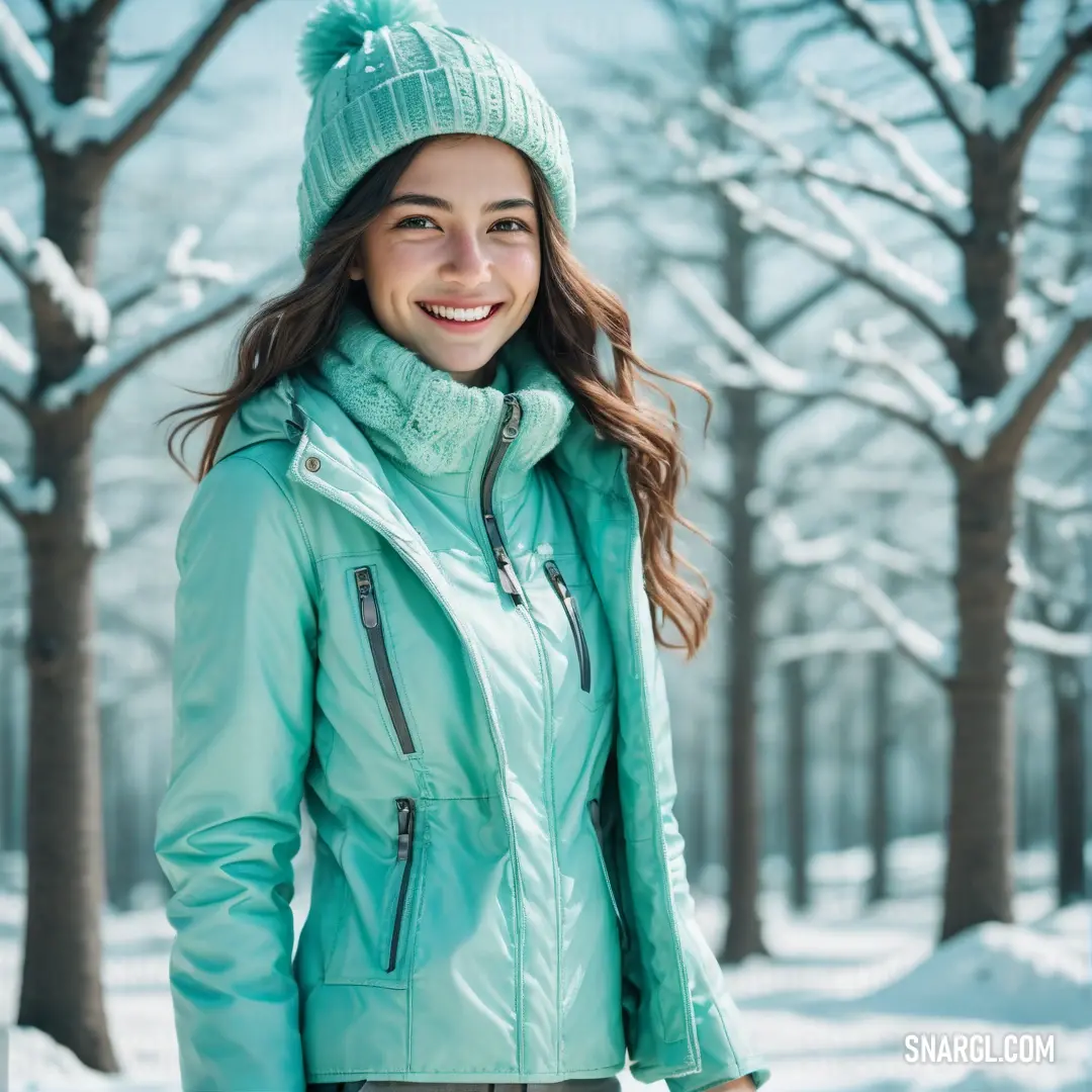 Woman in a green jacket and hat standing in the snow in front of trees and snow covered ground